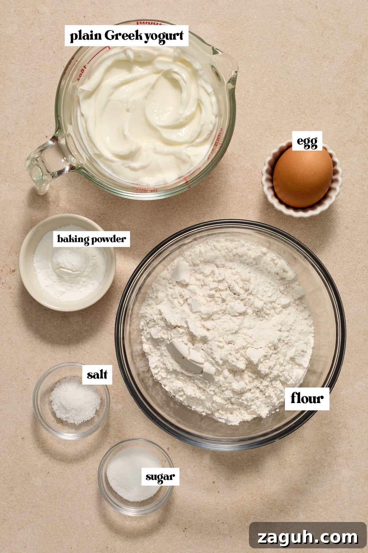 Flour, plain greek yogurt, egg and other ingredients to make recipe on surface.