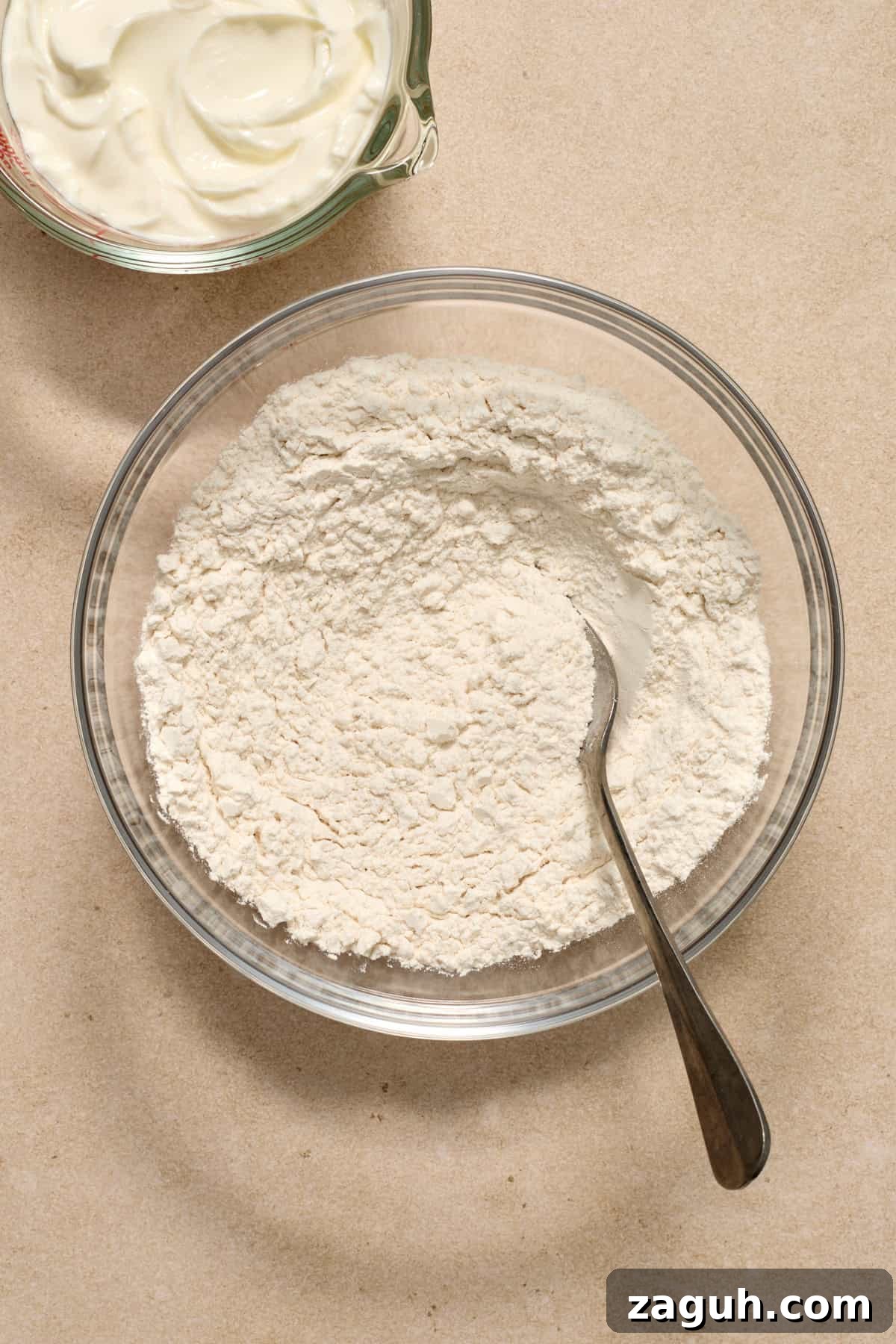 Dry ingredients in glass mixing bowl with spoon.