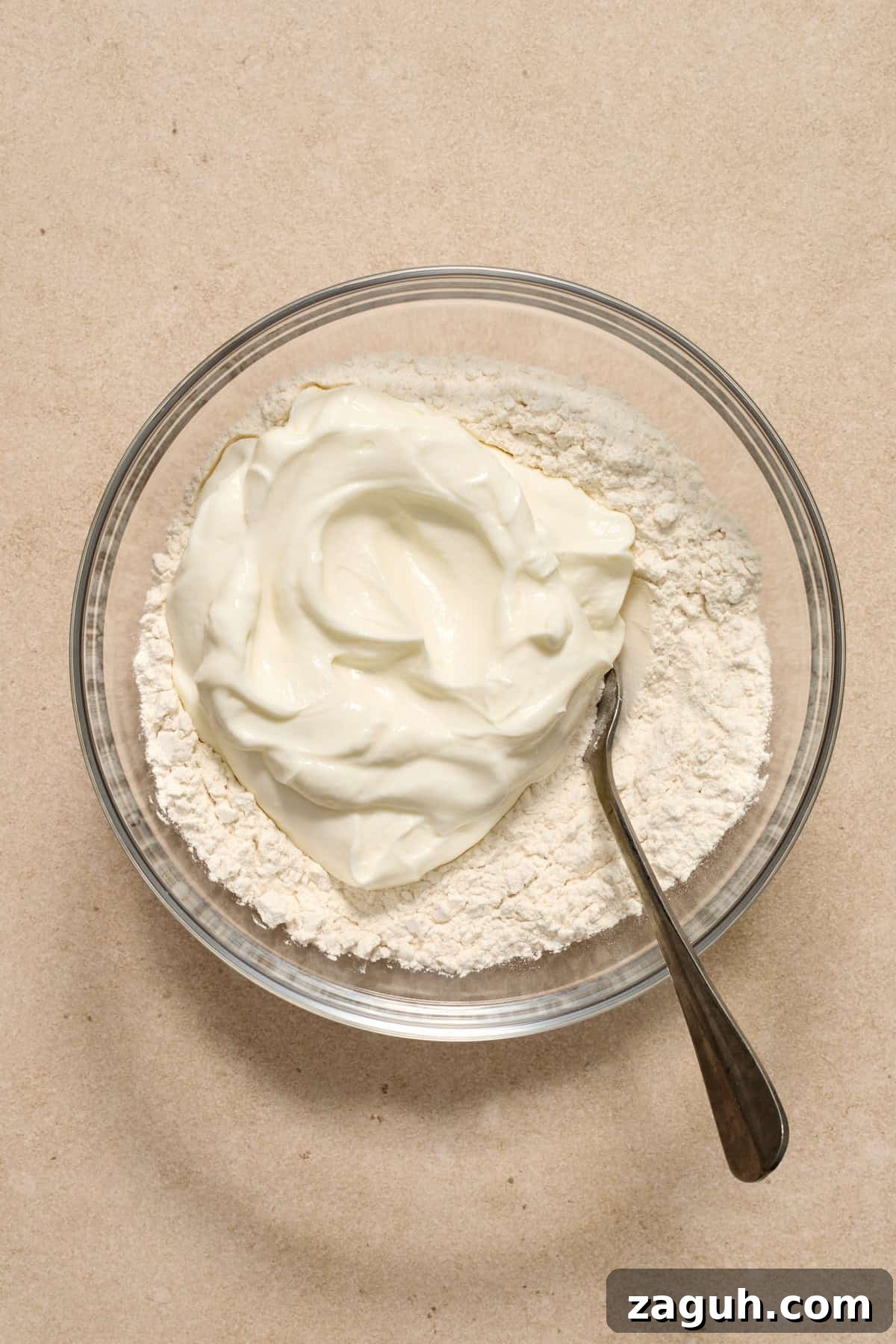 Greek yogurt added to bowl with flour and spoon.