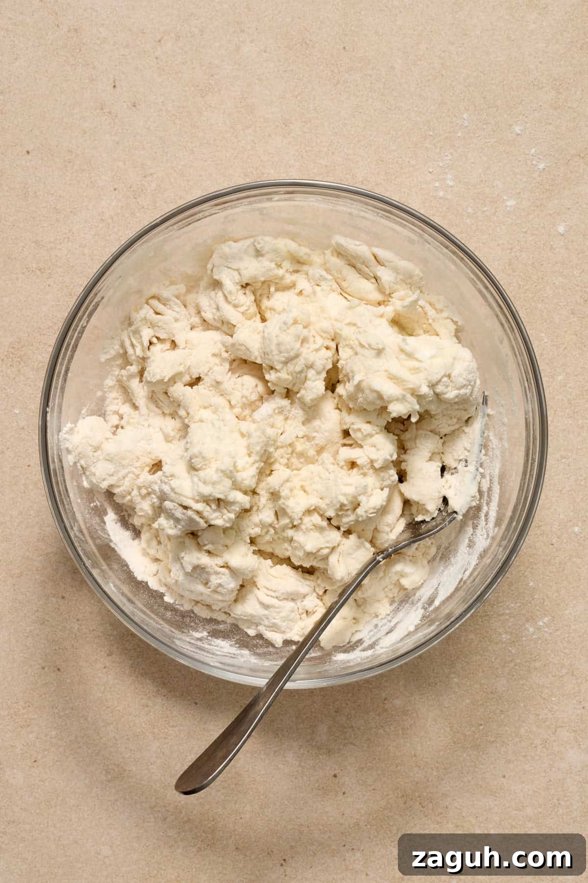 Greek yogurt bagel dough mixture in glass bowl with metal spoon.