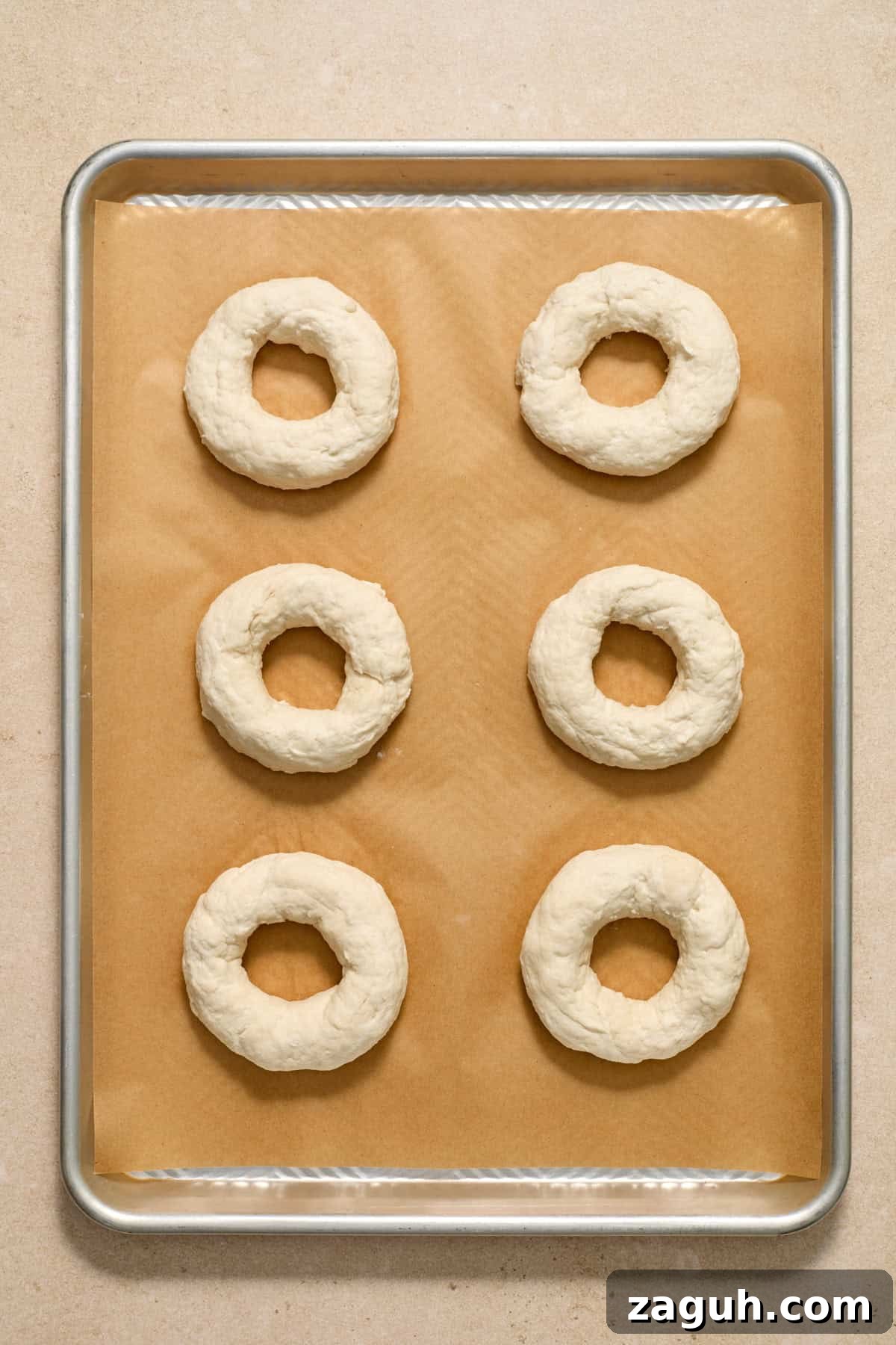 Bagels formed and arranged on parchment paper lined cookie sheet.