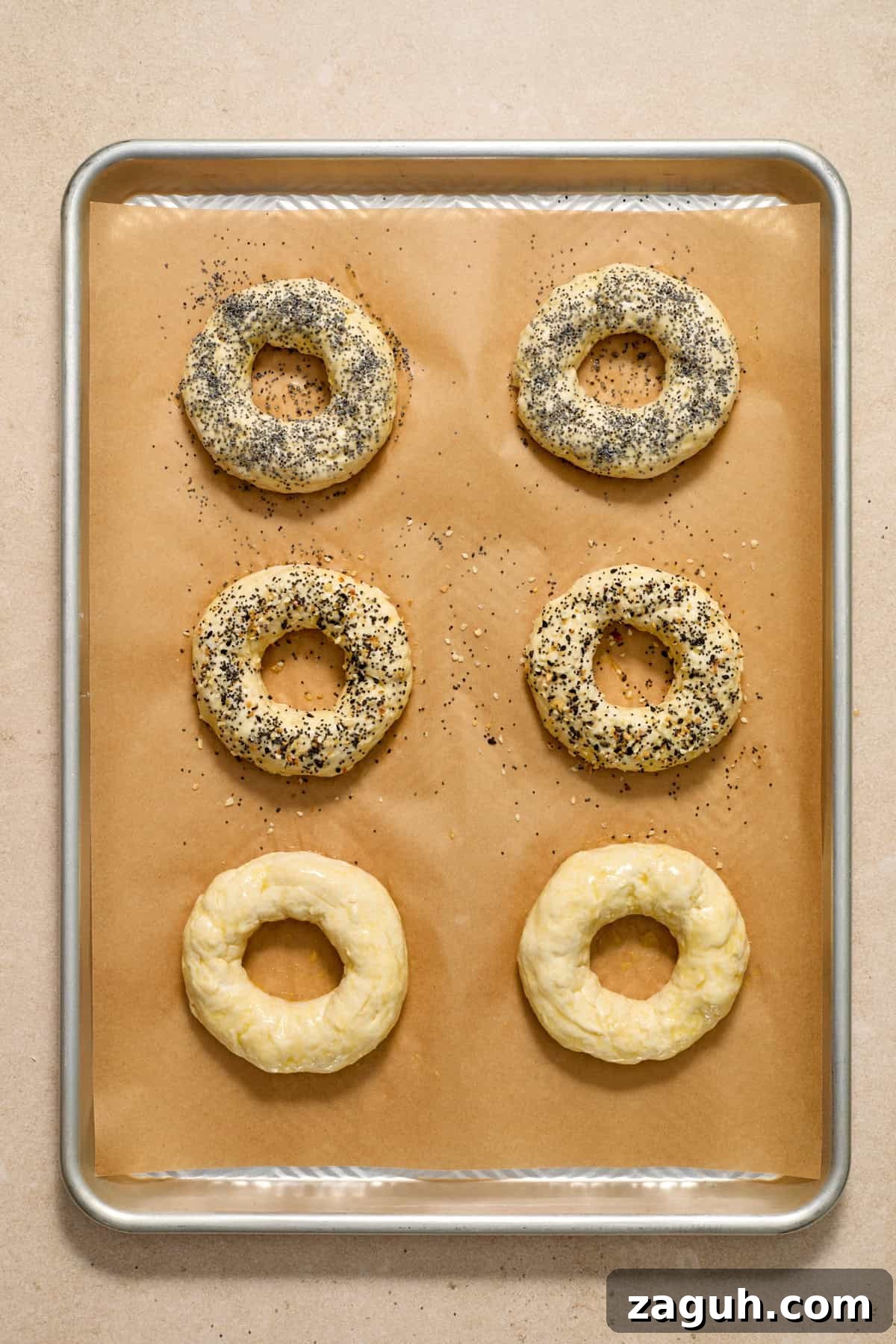 Egg washed bagels with poppy seeds and other ingredients on top.
