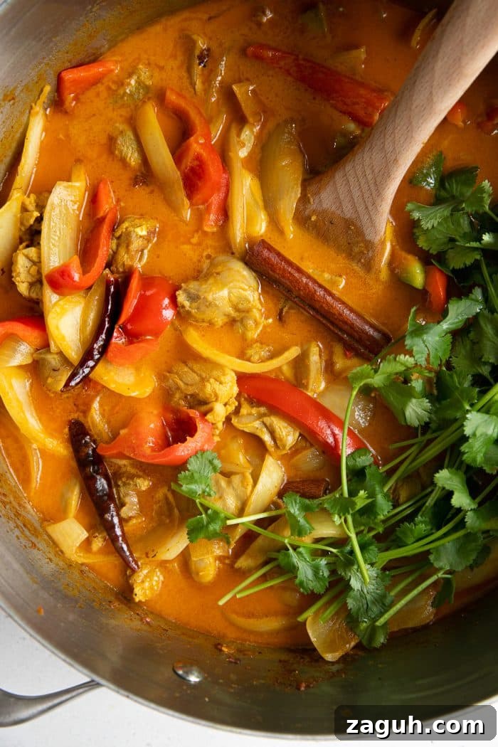 Chicken curry recipe in a large heavy-bottomed pan with aromatics, cilantro, and bell pepper.