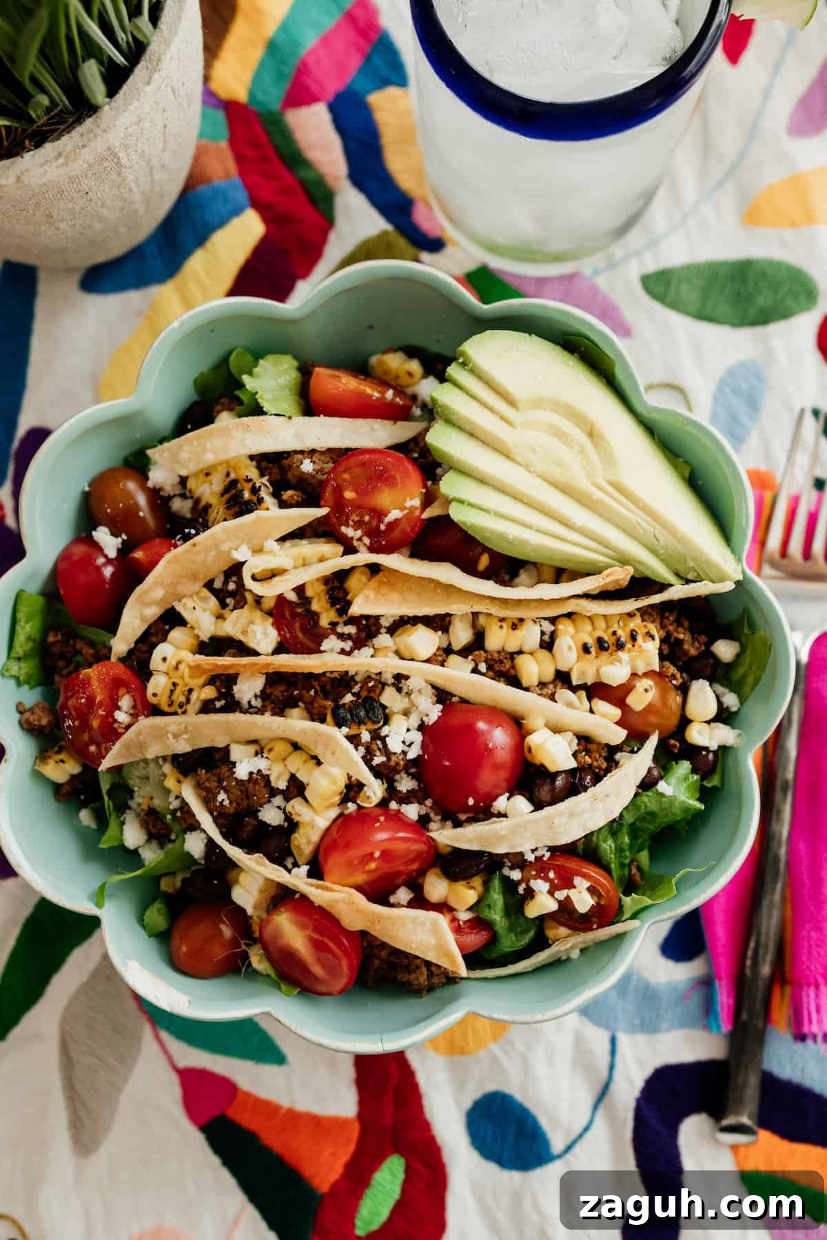 A healthy Taco Salad served in a turquoise bowl garnished with colorful toppings on a colorful Otomi runner