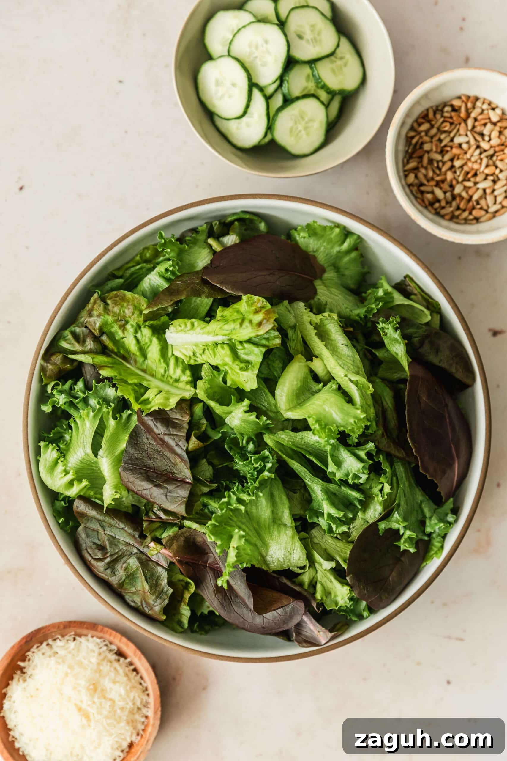 Green Salad with Sherry-Shallot Vinaigrette Recipe 3 White bowls of lettuce, sunflower seeds, and cucumbers on a beige counter next to a wood bowl of parmesan.