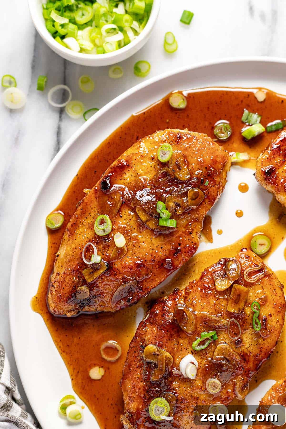 20-Minute Garlic Chicken with Honey Glaze 10 Close up of a large round plate with honey garlic chicken garnished with sliced green onion.