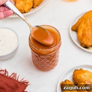 Classic Buffalo Sauce Recipe: Spicy Wing & Dip Sauce in Minutes 9 Orange sauce in a small jar, being spooned out, in front of plates of chicken wings.