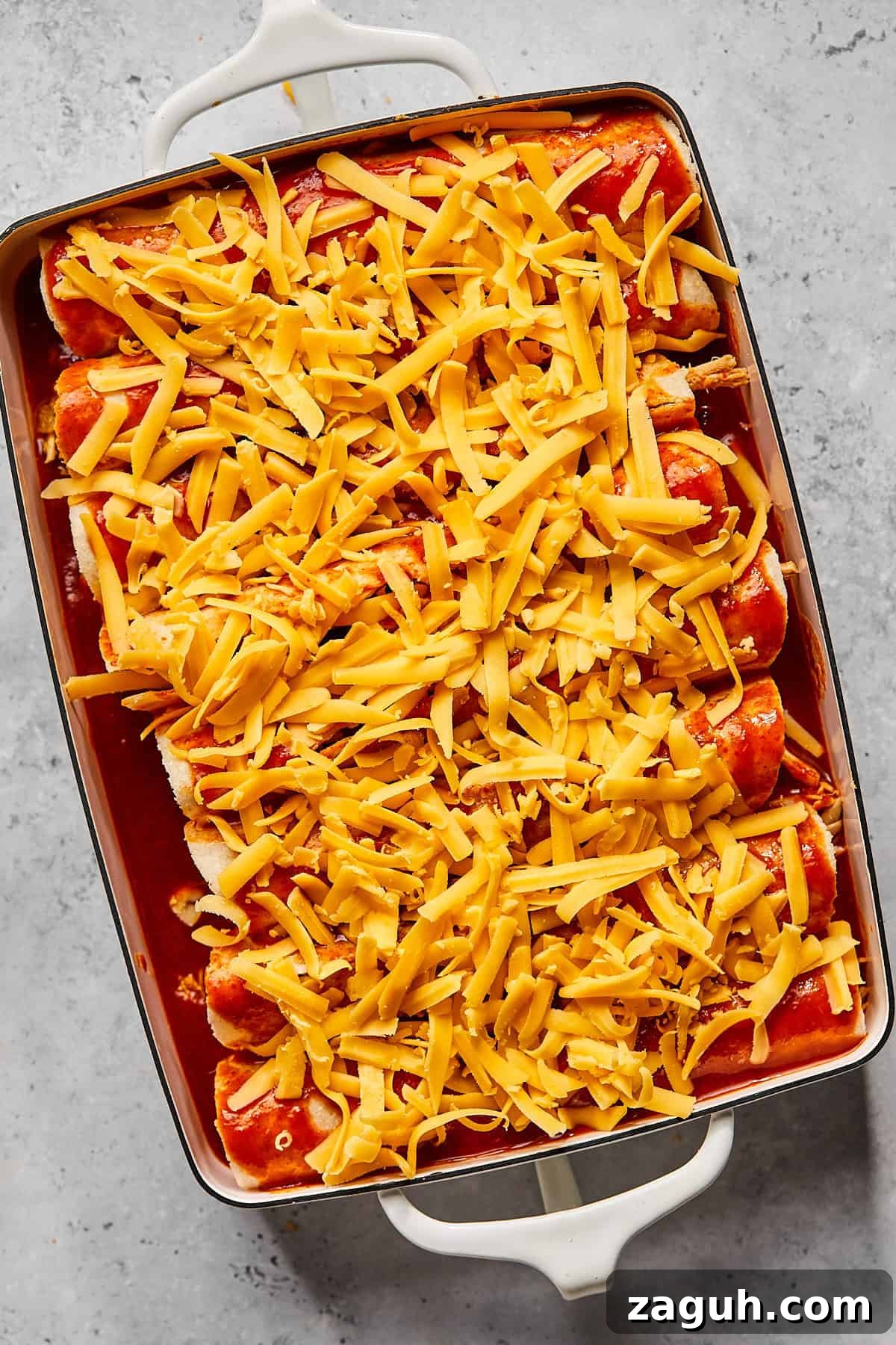 a casserole dish filled with tortillas and sauce and covered in shredded cheddar cheese 