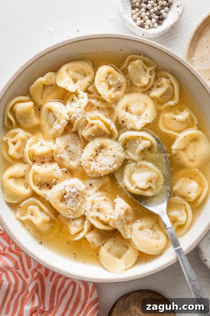 Tortellini in Rich Bone Broth Recipe: Comforting Italian Soup 2 Shallow bowl full of tortellini simmered in bone broth and garnished with fresh cracked black pepper and grated Parmesan cheese.