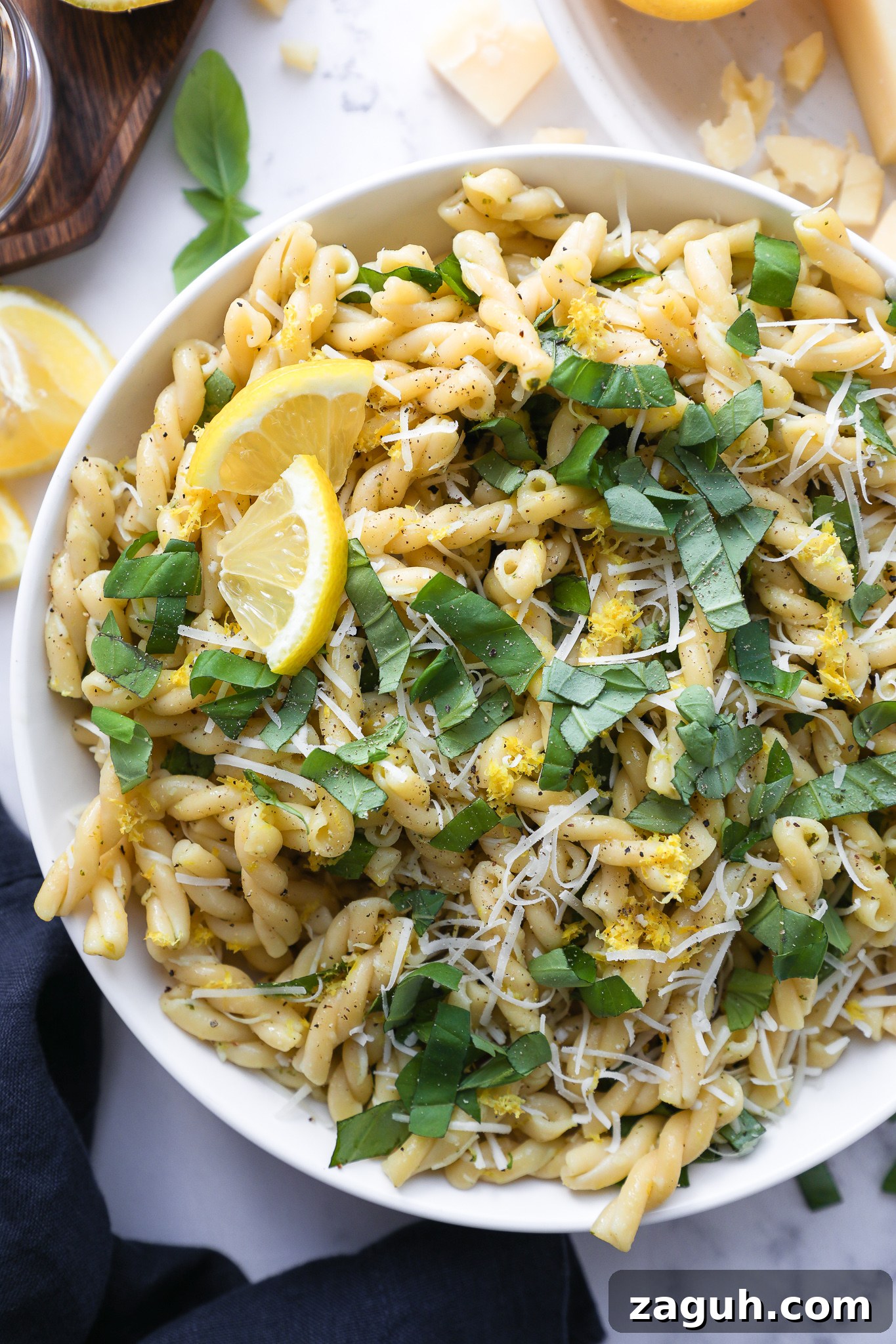 Lemon Basil Pasta Salad with Creamy Dressing and Fresh Herbs 5 Close photo of pasta salad made with lemon basil and parmesan cheese in a white bowl sitting next to a dark blue linen napkin
