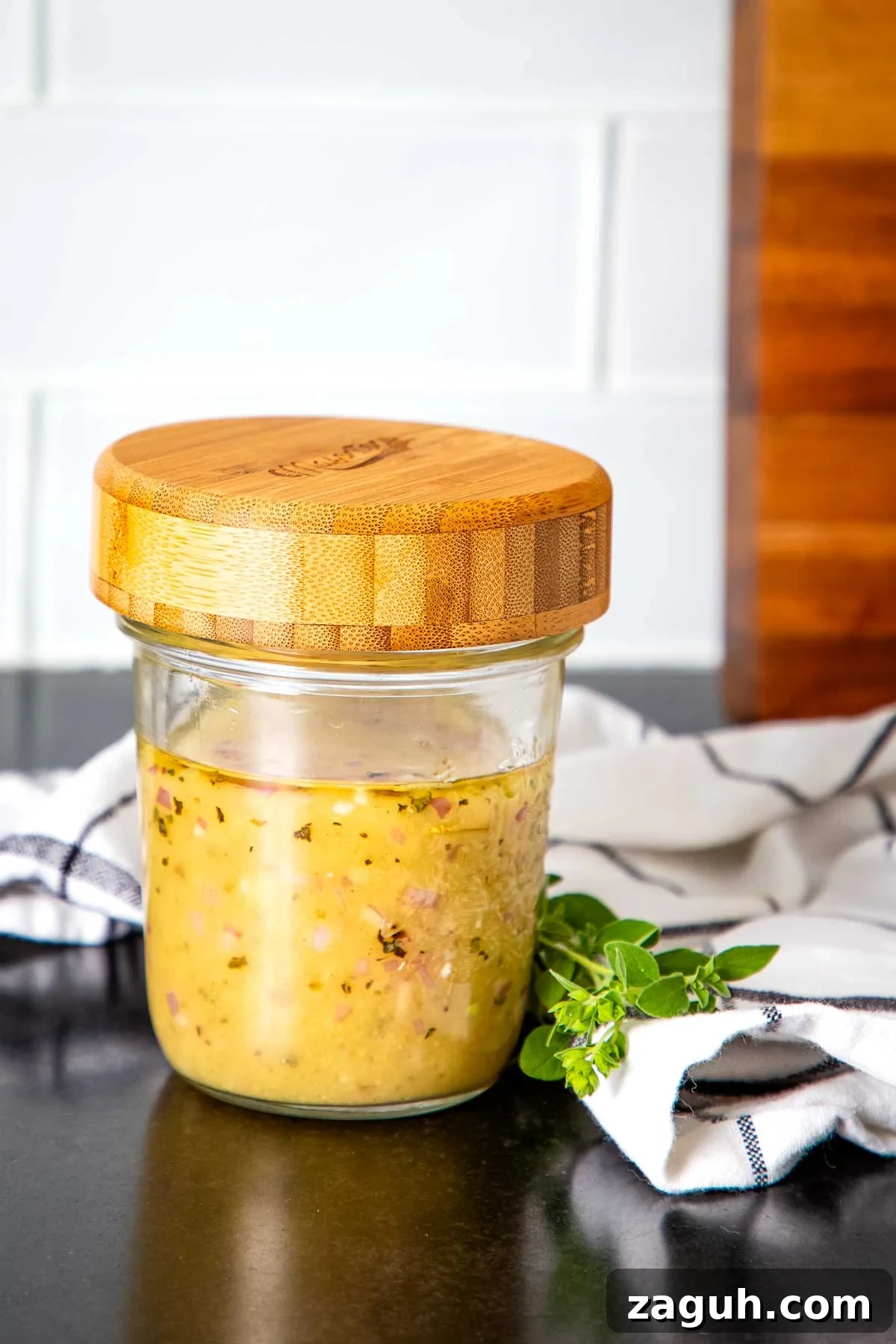 Jar of salad dressing that's yellow-ish with floating pieces of onion and spices.