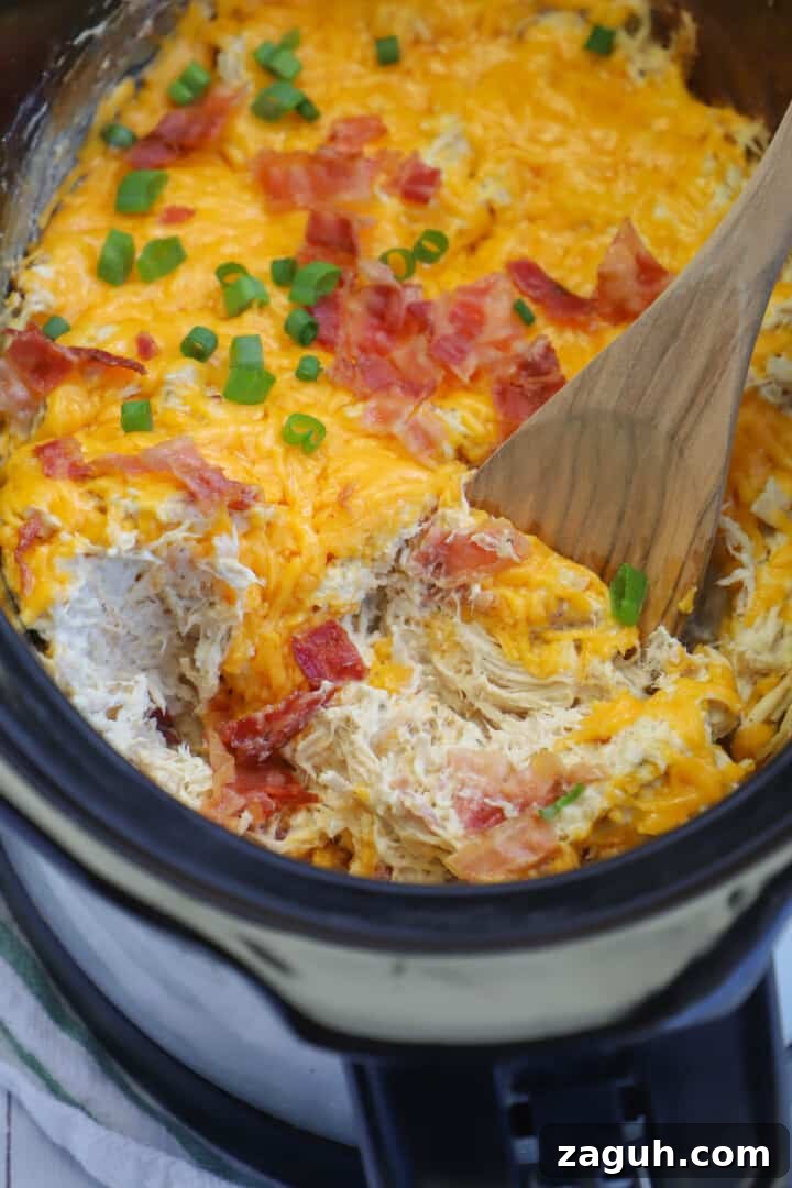 Creamy Slow Cooker Crack Chicken Recipe for Sandwiches & Dips 2 Slow Cooker Crack Chicken being mixed with a wooden spoon.