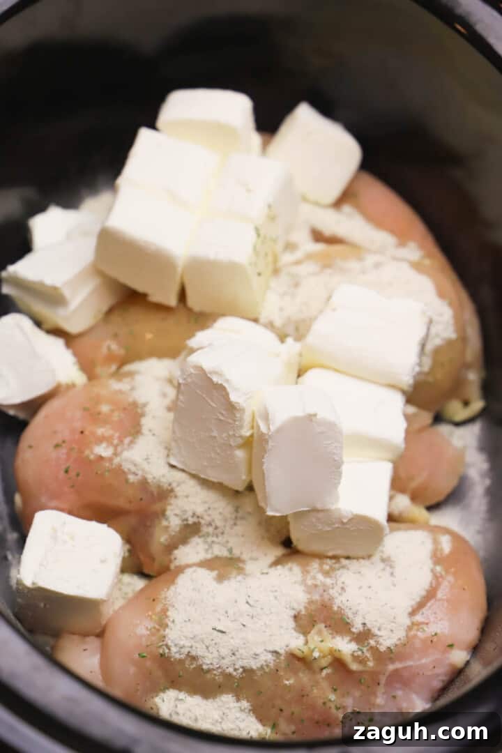 Creamy Slow Cooker Crack Chicken Recipe for Sandwiches & Dips 3 chicken, seasoning, and cubed cream cheese in slow cooker.