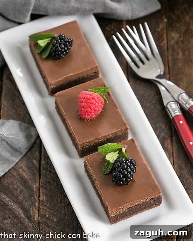 Decadent Chocolate Cheesecake Brownies Recipe 3 Ovehead view of 3 cheesecake brownies on a white tray topped with fresh berries.