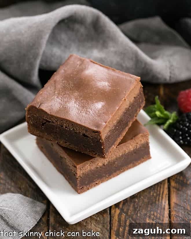 2 cheesecake brownies stacked on a square white dish