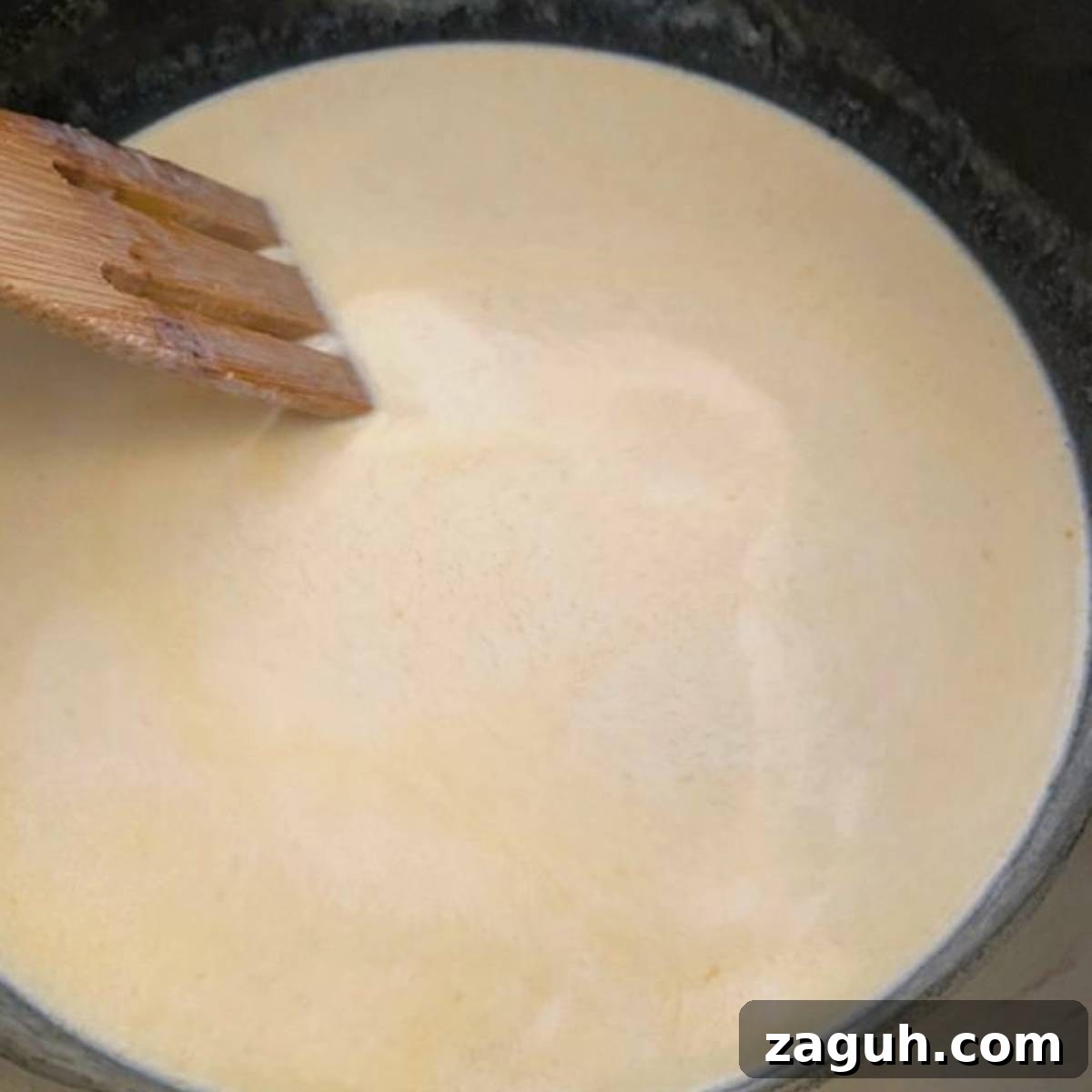 Creamy White Cheddar Mac and Cheese Recipe for Dinner 6 Wooden spoon stirring cream in skillet.