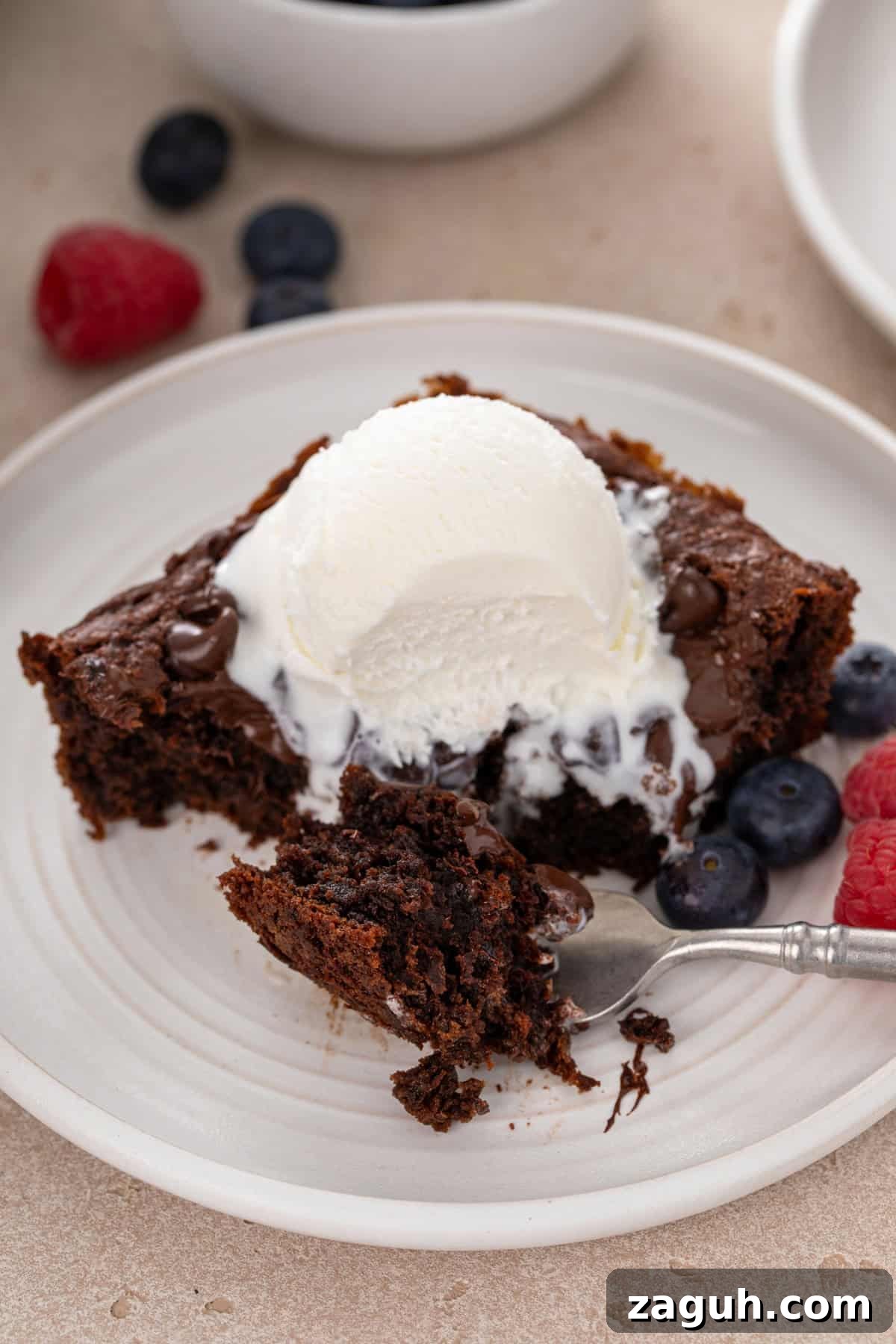 Decadent Chocolate Dump Cake Recipe That Melts in Minutes 11 Fork holding a bite of chocolate dump cake next to a slice of the cake on a white plate.