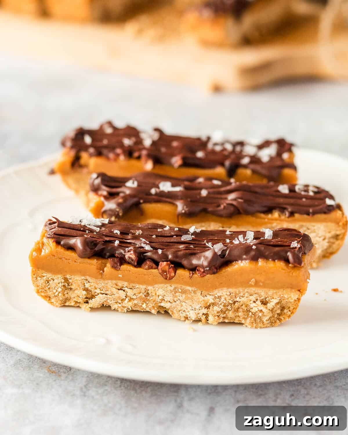 Peanut Butter Millionaire Shortbread Recipe: Decadent Layered Dessert 3 Three millionaires shortbread bars on a white plate. There are some more in the background.