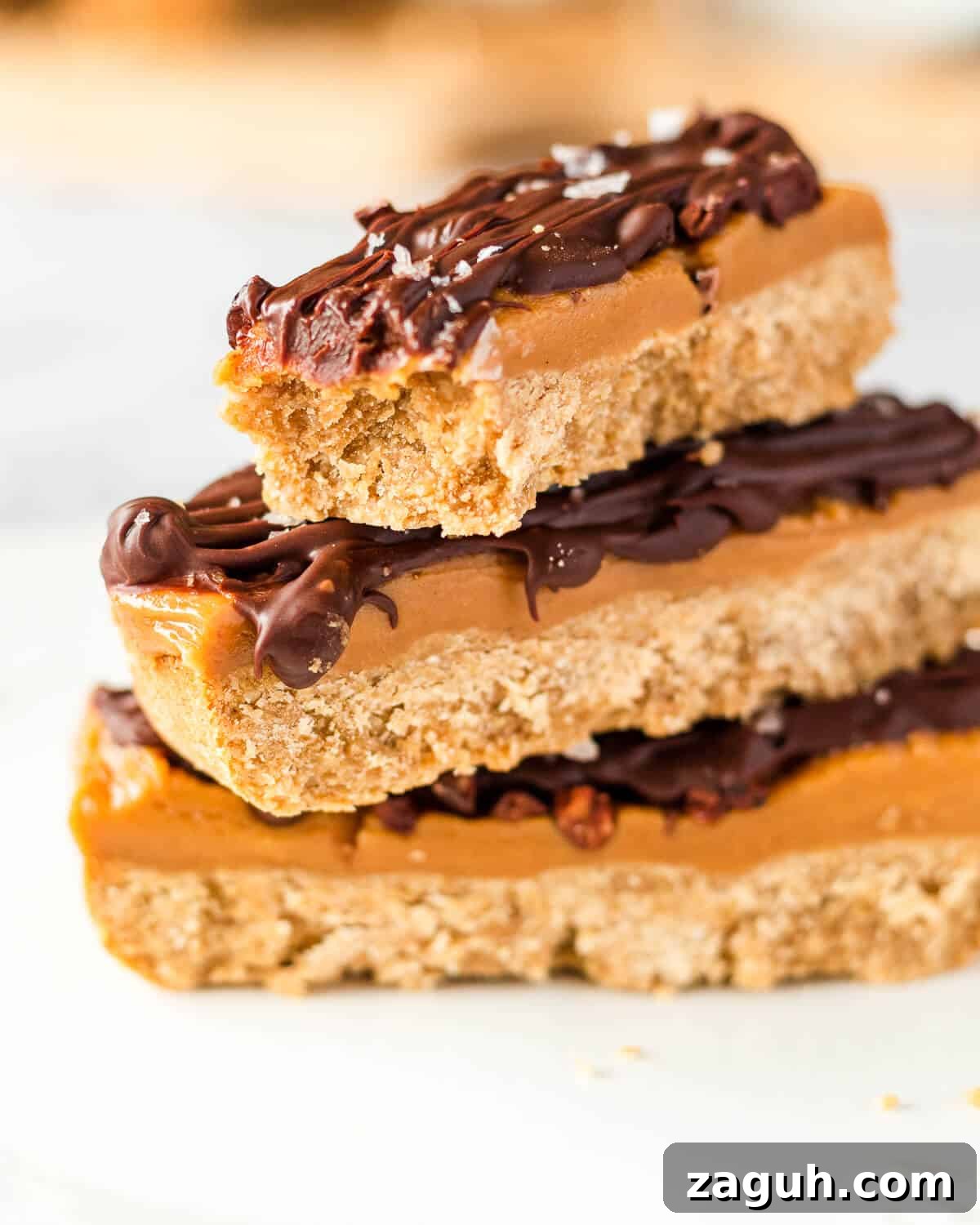 Peanut Butter Millionaire Shortbread Recipe: Decadent Layered Dessert 4 Three vegan millionaires shortbread bars stacked on top of each other, a bite has been taken from the top one.
