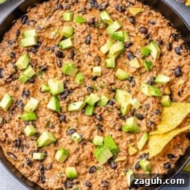 Spicy Chili Cheese Dip Recipe for Parties and Game Day 13 chili dip in a skillet topped with green onions and avocado.