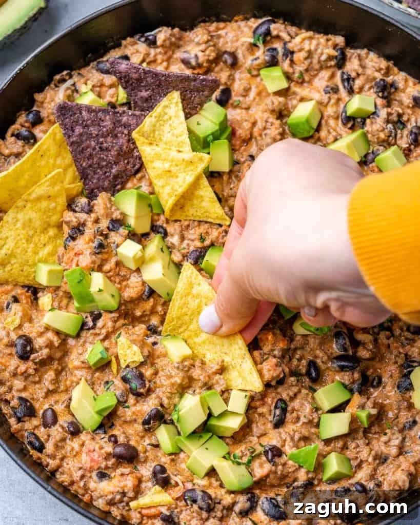 Spicy Chili Cheese Dip Recipe for Parties and Game Day 3 Woman's hand dipping a chip into a cheesy dip.