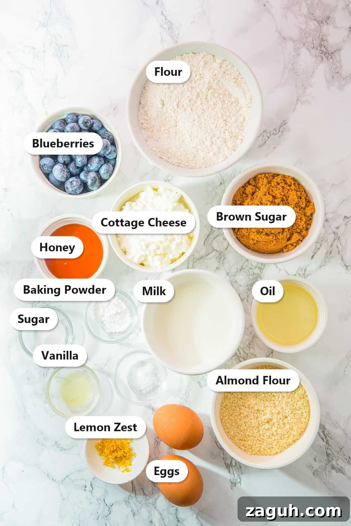 Labeled ingredients for Cottage Cheese Blueberry Muffins, including flour, blueberries, cottage cheese, brown sugar, honey, milk, oil, baking powder, sugar, vanilla, almond flour, lemon zest, and eggs.