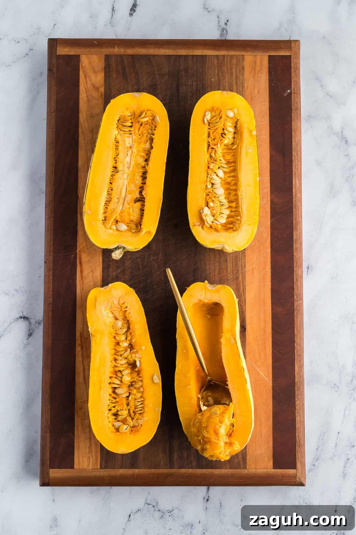 A spoon scooping seeds out of the center of a half of squash.