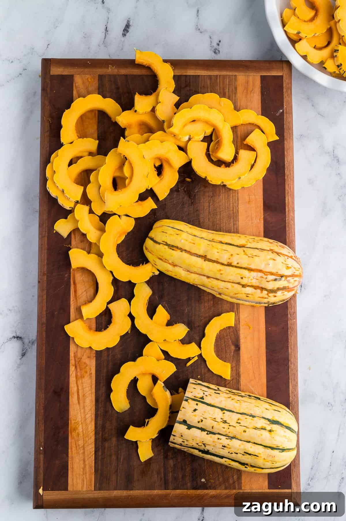 Sliced delicata squash on a wooden cutting board.