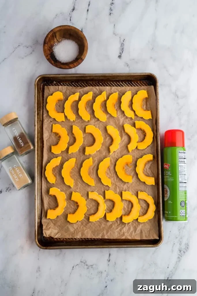 Sliced delicata squash on a baking sheet with seasonings around it.