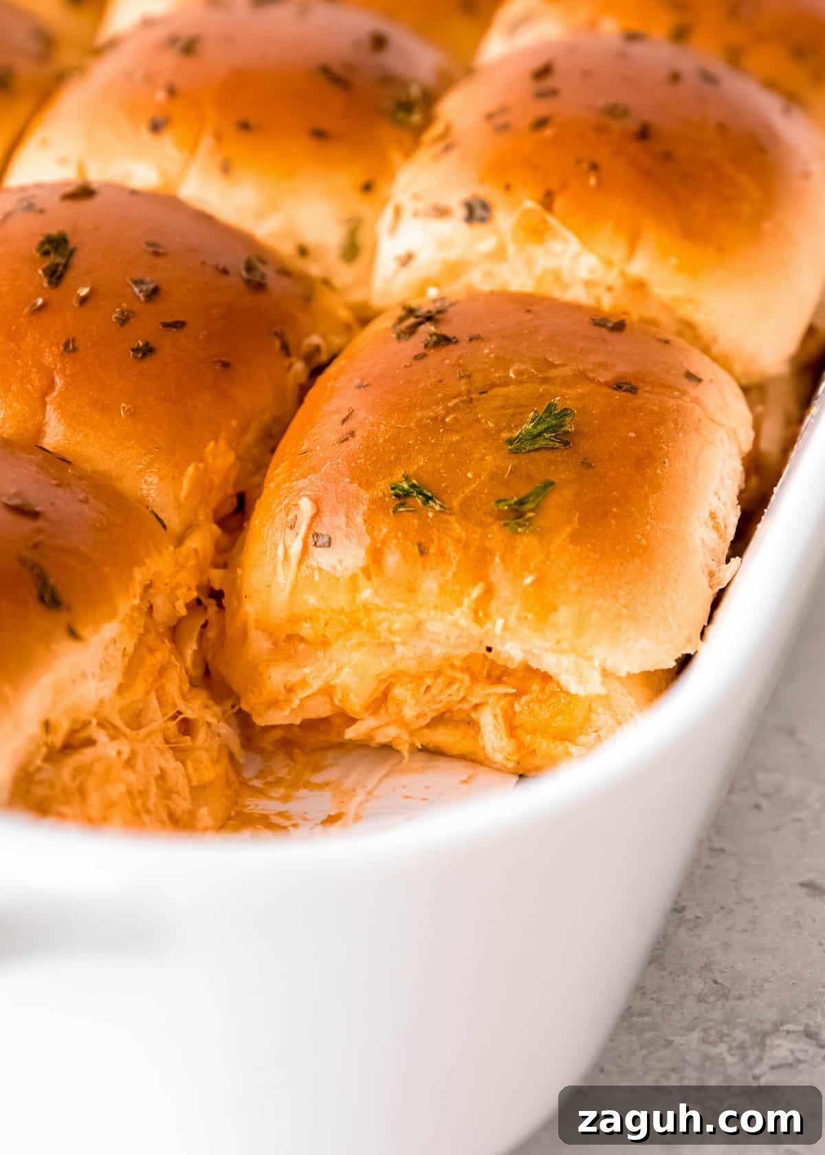 Spicy Buffalo Chicken Sliders with Blue Cheese Slaw 13 a baking dish full of baked buffalo chicken sliders, sprinkled with herbs