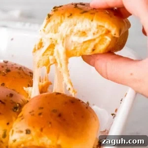 Spicy Buffalo Chicken Sliders with Blue Cheese Slaw 16 a hand grabbing a buffalo chicken slider from a casserole dish; gooey, melted cheese strings down
