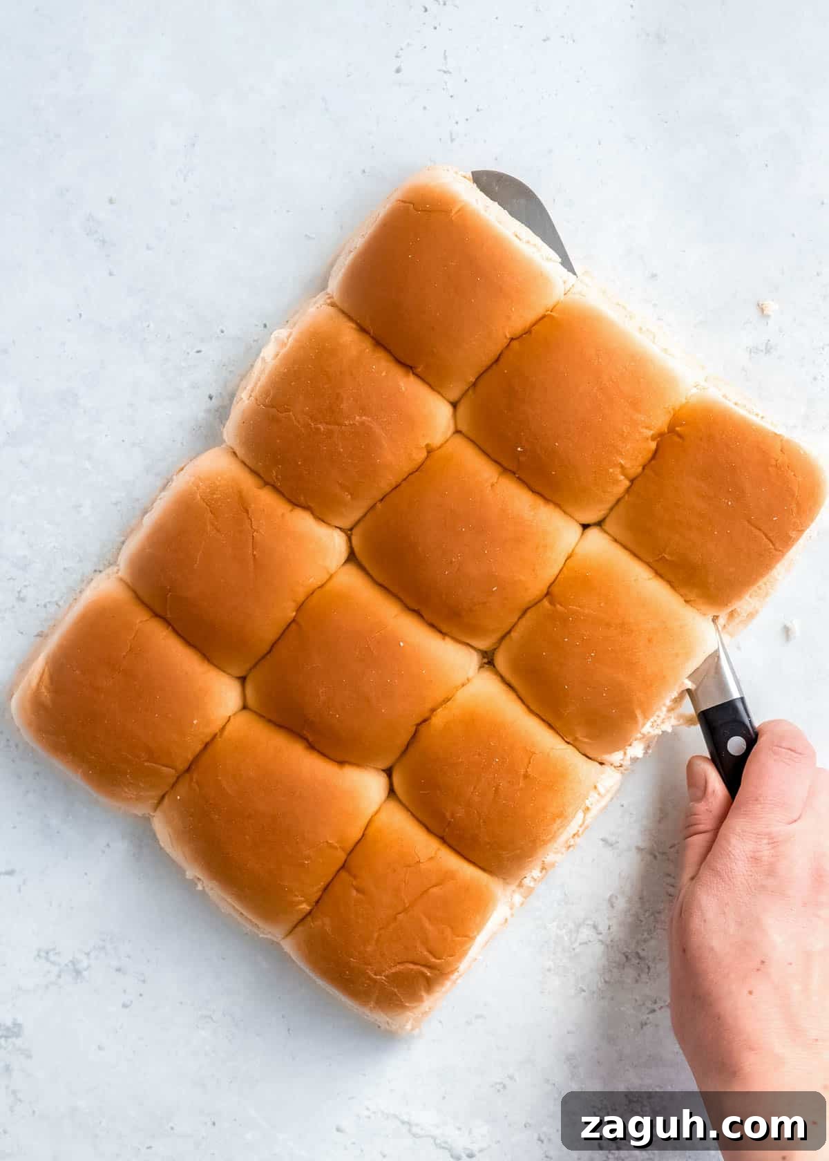 Spicy Buffalo Chicken Sliders with Blue Cheese Slaw 7 a hand using a knife to slice the buns in half, parallel to the countertop