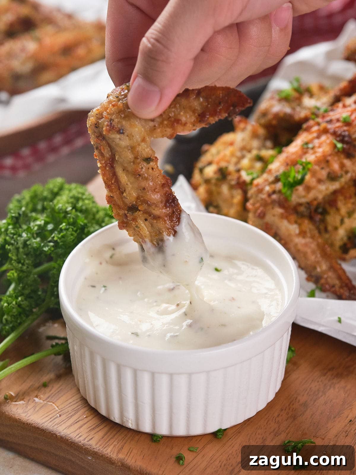 Carnivore Lunch Ideas for Simple Weekly Meal Planning 7 A hand dips a parmesan chicken wing into a small white bowl of creamy sauce.