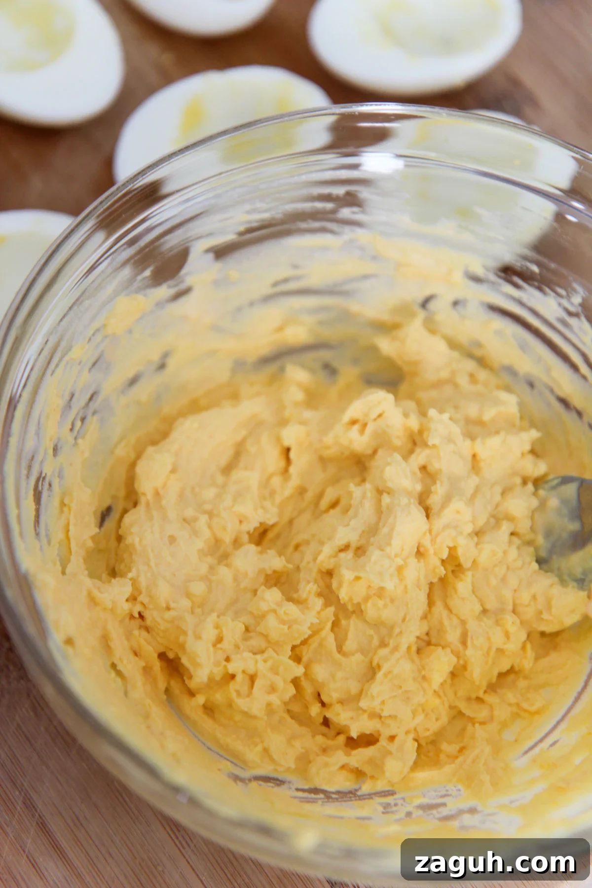 Perfect Classic Deviled Eggs Recipe for Parties and Holidays 3 egg yolk mixture in a clear bowl and egg whites in the background