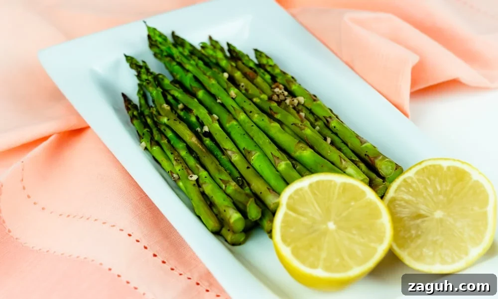 Lemon Oven-Roasted Asparagus on white plate with a sliced lemon Lemon Oven-Roasted Asparagus on white plate with a sliced lemon.