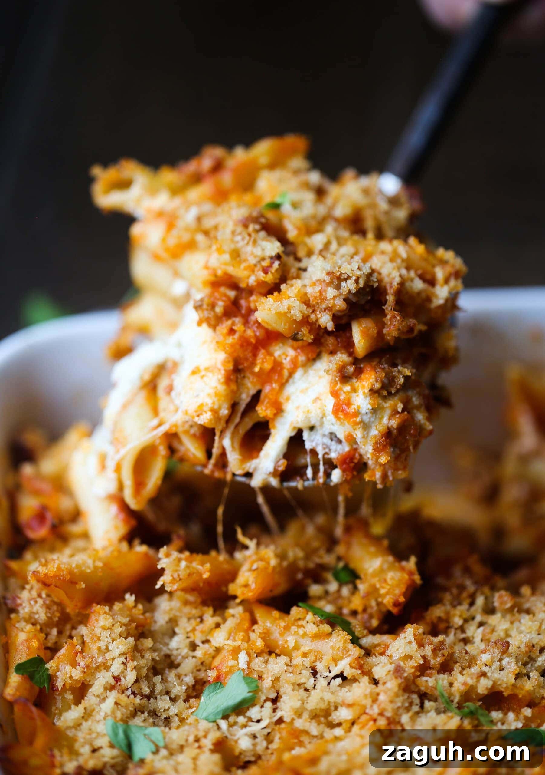 Creamy Baked Mostaccioli with Melted Cheese 2 A spoonful of cheesy baked mostaccioli is served from a casserole dish.