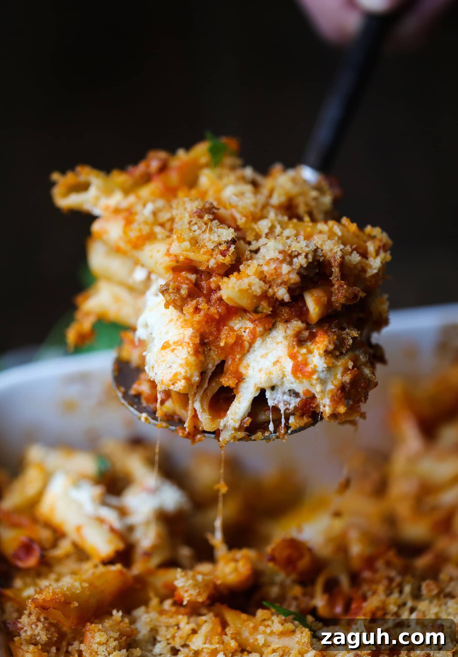 Creamy Baked Mostaccioli with Melted Cheese 15 A spoonful of cheesy baked mostaccioli is served from a casserole dish.