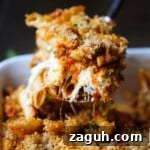 A spoonful of cheesy baked mostaccioli is served from a casserole dish.