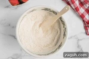 Fresh Strawberry Sourdough Muffins Recipe for Soft, Tangy Loaves 4 Mixing bowl with dry ingredients and a wooden spatula, with fresh strawberries on the side.