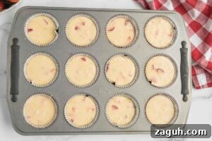 Fresh Strawberry Sourdough Muffins Recipe for Soft, Tangy Loaves 7 Muffin tin filled with batter, ready to be baked, with a red and white checkered cloth and fresh strawberries nearby.