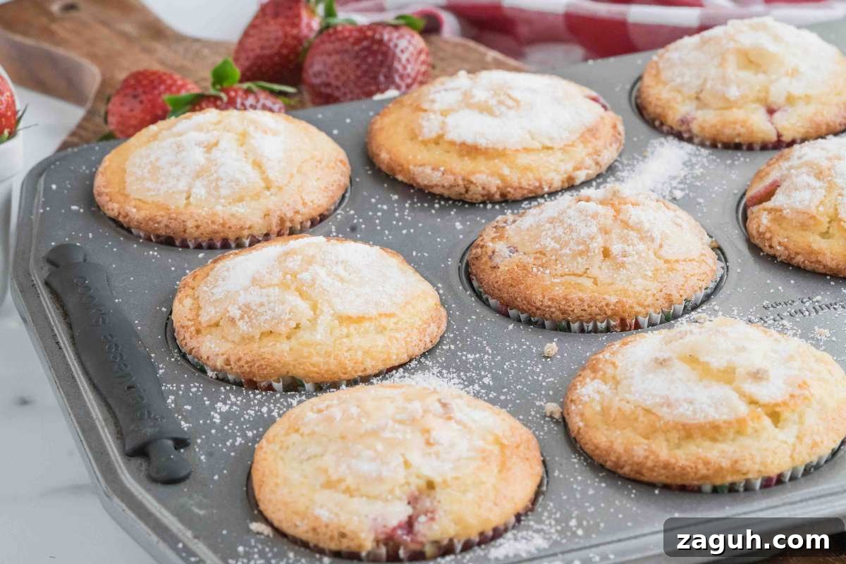 Fresh Strawberry Sourdough Muffins Recipe for Soft, Tangy Loaves 10 A muffin tin filled with freshly baked muffins, topped with sugar, with fresh strawberries and a red and white checkered cloth in the background.