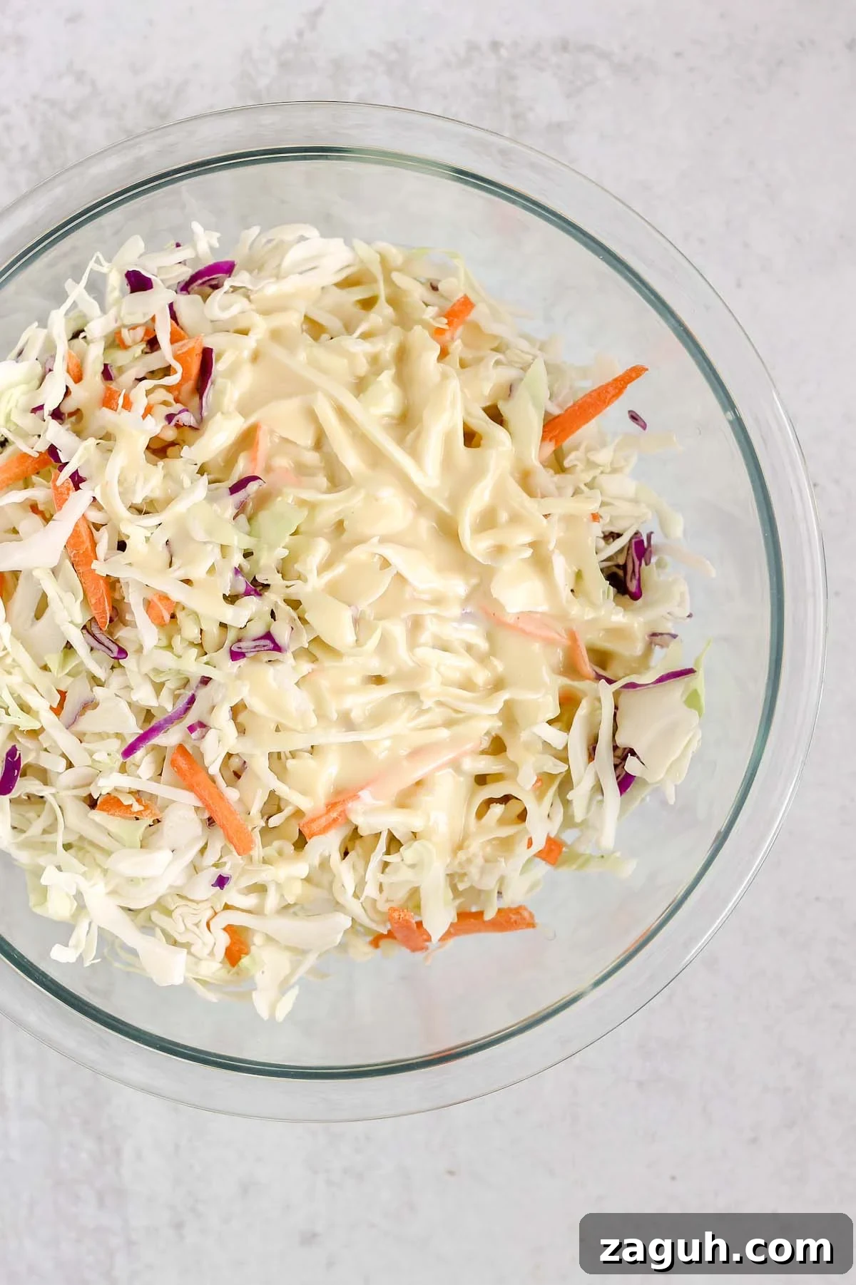 Creamy Paleo & Whole30 Coleslaw Recipe for Simple Sides 5 Dressing poured on coleslaw mix in a mixing bowl.
