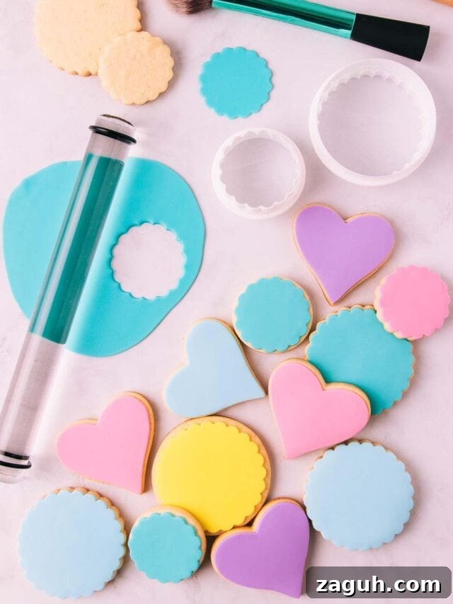 Stamped Fondant Cookies: Step-by-Step Guide for Beautiful Designs 3 Round and heart shaped cookies covered in shades of pastel fondant, on a grey marble surface, with some of the tools needed to decorate sugar cookies with fondant.