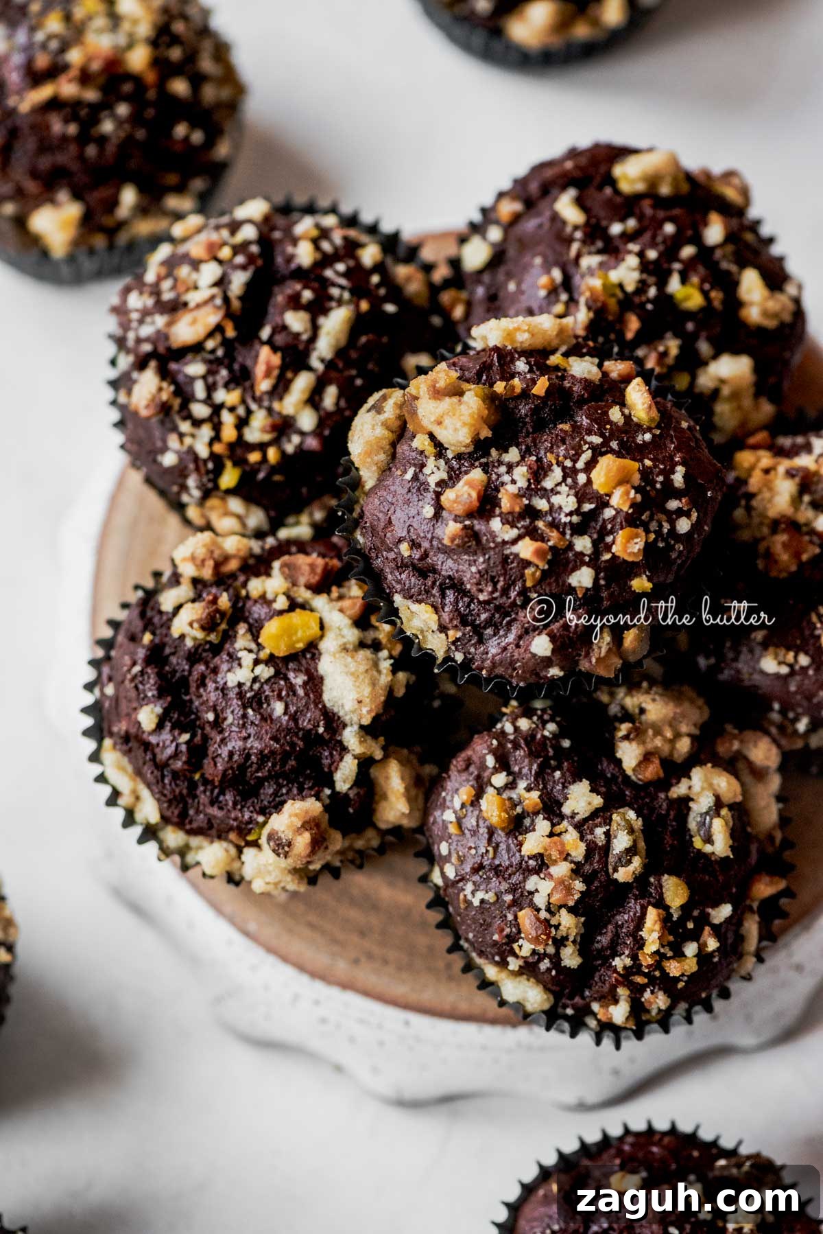 Dark Chocolate Pistachio Cream Cheese Muffins Recipe 6 Small plate of dark chocolate pistachio cream cheese muffins on gray background | All Images © Beyond the Butter®
