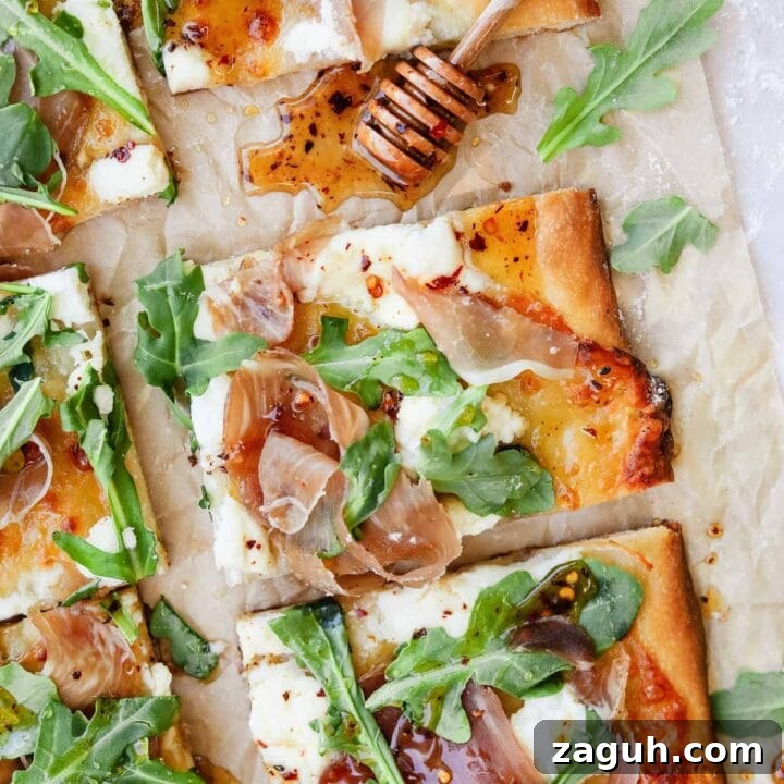 Prosciutto ricotta pizza with arugula and hot honey on parchment paper wit honey dripper.