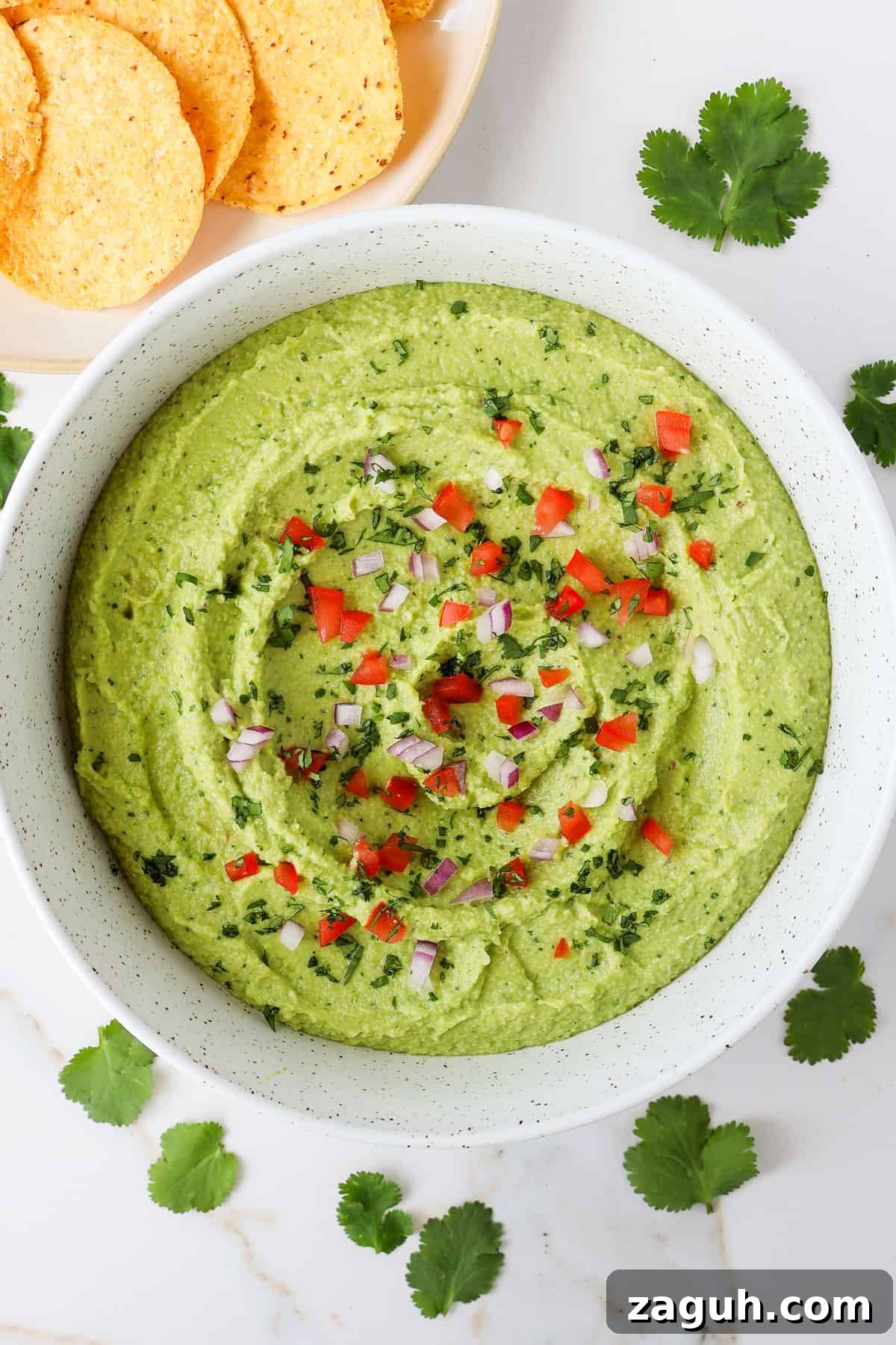 Protein-Packed Edamame Guacamole Recipe for Muscle Fuel 9 Guacamole in a bowl with diced tomatoes and onions on top.