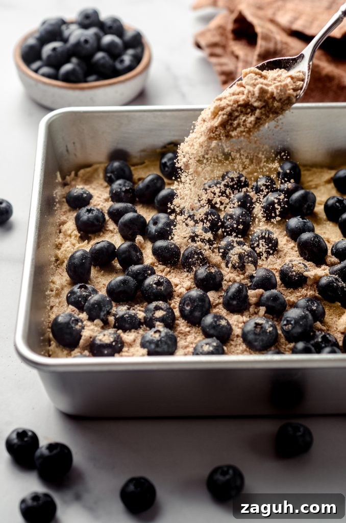 Moist Blueberry Sour Cream Coffee Cake Recipe 15 Someone is dropping streusel topping onto blueberry coffee cake before baking.