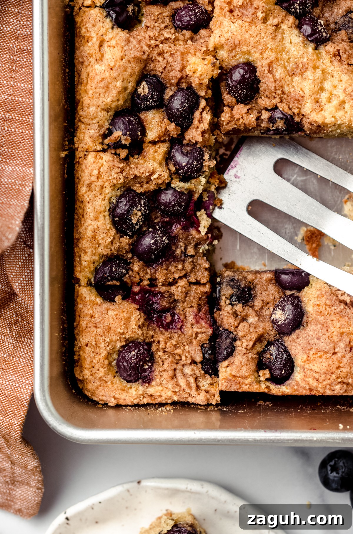Moist Blueberry Sour Cream Coffee Cake Recipe 22 Aerial photo of sliced blueberry coffee cake in a pan with a serving spatula.