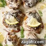 close up, overhead shot of crockpot creamy lemon dill chicken on a white platter garnished with lemon slices & fresh dill