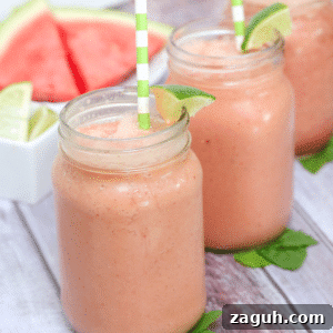 Dairy-Free Watermelon Protein Smoothie Recipe for Summer Energy 4 Three mason jars filled with watermelon smoothie and topped with green straws and lime sitting on mint leaves and fresh watermelon behind them